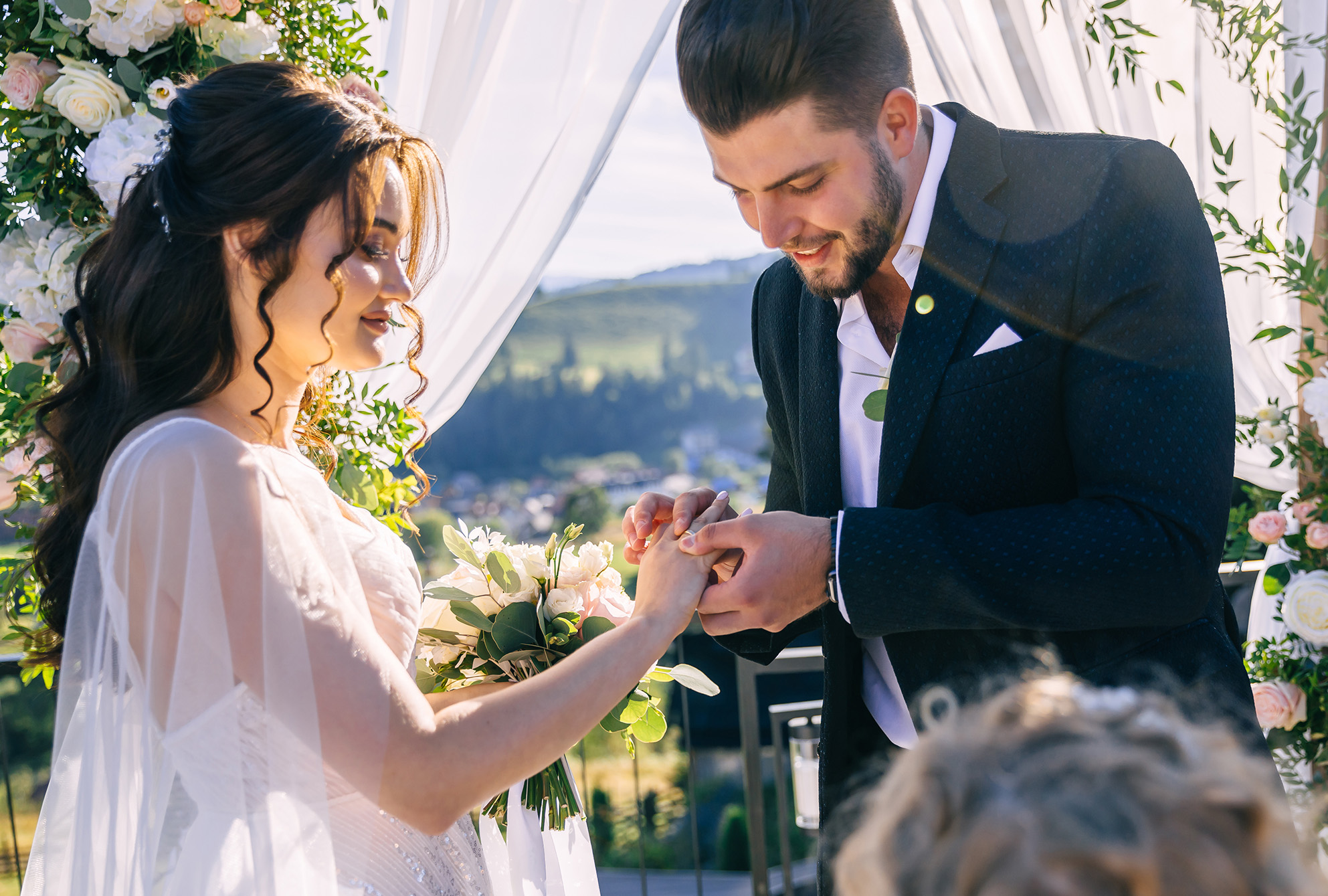 Groom putting wedding ring on bride's finger during wedding ceremony